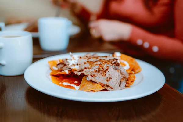 Bir restoranda bir tabak kremalı, peynirli ve kırmızı soslu chilaquiles servis ediyorlar, lezzetli bir Meksika yemeği..