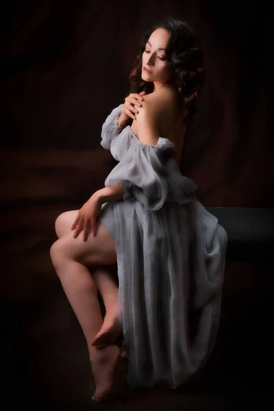Beautiful latin woman in an antique dress, she is posing sitting she is very comfortable, with black background, low key photography with spot light.