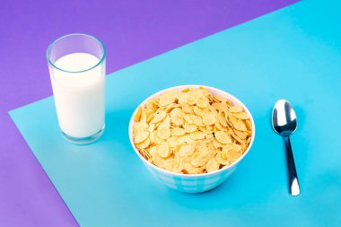 View of a plate with natural cereal and a glass of fresh milk against a background of pastel colors.