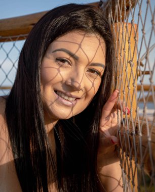 Yüzünde güneş ve mavi gökyüzü olan bir plaj girişindeki hamağın gölgesinde poz veren esmer model. Gelişigüzel, tatil ve fotoğraf pozlarından bahsediyor..