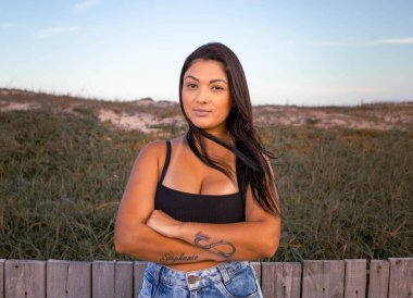 Kumsal kaldırımında duran esmer model ciddi bir ifade ve tavırla. Mavi kot şort giyiyor ve mavi renkli bir fotoğrafta siyah kesilmiş. Tatilden ve rahatlıktan bahset.