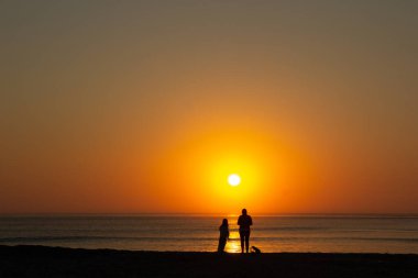 Gün batımına bakıyorum. Barra plajı, Aveiro, Portekiz. Kumsalda bir yetişkinin ve bir çocuğun kırmızı güneşi ve silueti.