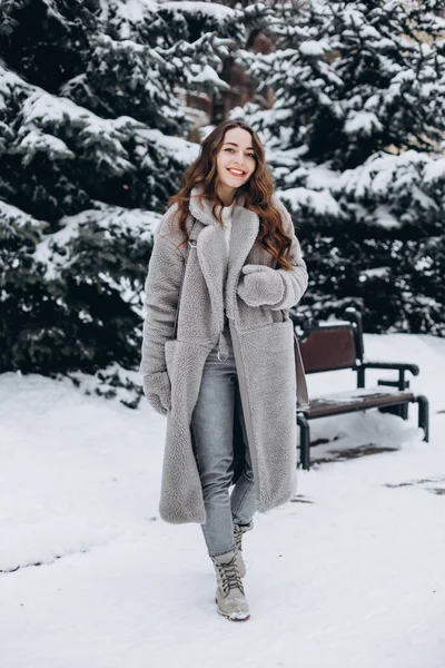 雪の公園を歩いている可愛い女性の肖像画が喜んで笑いながらコートを着てミトン — ストック写真