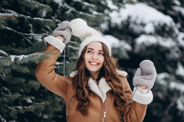 在冬天的森林里 快乐的女孩穿着温暖的棕色夹克 头戴白帽 对着相机微笑 — 图库照片