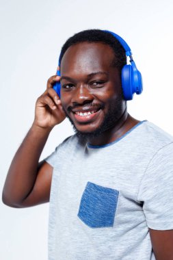 Erkek bir aktör kameraya gülümsüyor. Kafasında kulaklık var. Mavi göğüs cebi olan gri bir gömlek giyiyor..