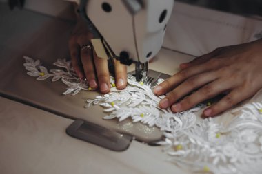 Makinenin yardımıyla zanaatkar yeni bir süs yapıyor. Süs, gelecekteki gelinliğin bir parçası. Süs beyazdı..