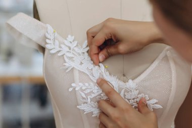 Bir kadın bir şey dikiyor ve süsünü mükemmelleştiriyor. Sarı bir iğnesi var. Süs beyazdı..