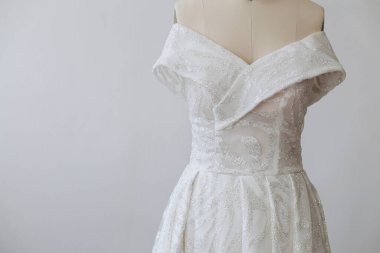 Beyaz arka plandaki mankenin üzerinde beyaz güzel bir elbise var. İlginç ve güzel bir süsü var. Pulları görebiliyoruz.