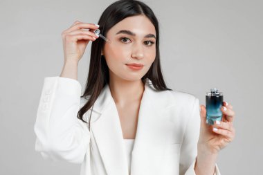 Genç ve güzel bir kozmetik uzmanının portresi beyaz bir odada yüzüne pipette ile su döktü.