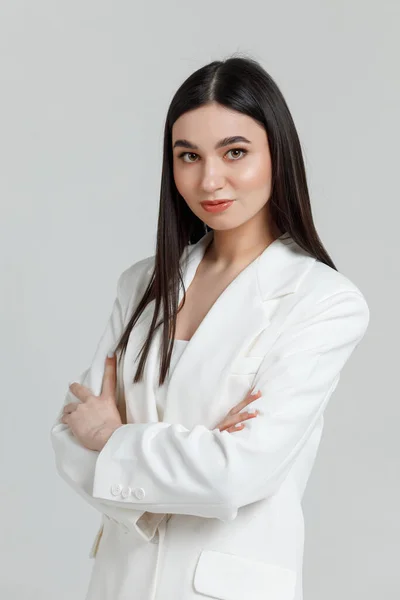 Beyaz takım elbiseli, gülümseyen ve kameraya bakan güzel bir esmer mankenin portresi.