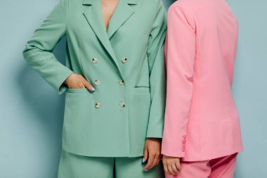 Mavi duvarın önünde renkli takım elbiseli iki güzel kadın mankenin grup fotoğrafı.