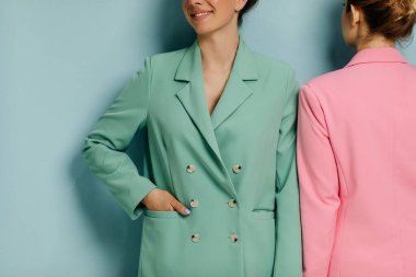 Mavi duvarın önünde renkli takım elbiseli iki güzel kadın modelin portresi.