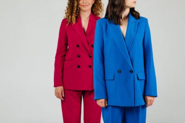 Beyaz duvarın önünde renkli takım elbiseli iki güzel ve mutlu kadın modelin fotoğrafı.