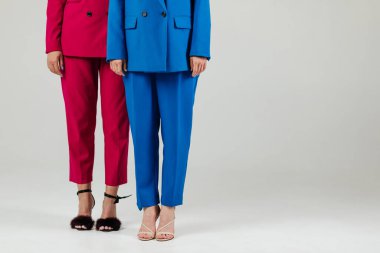 Beyaz duvarın önünde renkli takım elbiseli iki genç ve mutlu kadın modelin düşük bir fotoğrafı.