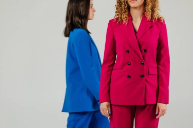 Beyaz duvarın önünde mavi ve kırmızı elbiseli iki mutlu kadın modelin portresi.