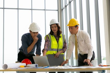 Mühendislerden oluşan bir takım mimar çalışma masasında duruyor ve inşaat planları üzerinde çalışıyor. Mühendisler konuşuyor.
