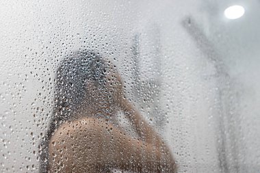 Genç Asyalı kadın aynaya yansıyan buhar yüzünden bulanık. Odaklanmamış bulanık arkaplan.