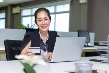Ofiste dizüstü bilgisayardan satın alan güzel Asyalı bir kadın ve ödeme için kredi kartıyla online laptop ekranı alışverişi yapıyor..