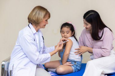 Genç bir kadın pediatrist küçük bir kızın aşısını gerçekleştiriyor. Doktora bak..