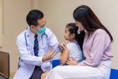 Genç bir kadın pediatrist küçük bir kızın aşısını gerçekleştiriyor. Doktora bak..