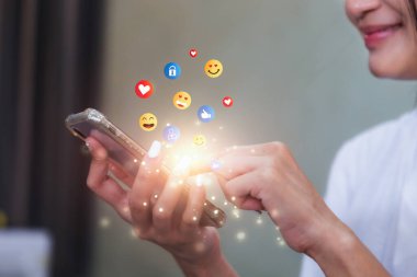 Akıllı telefon kullanıp emoji gönderen genç bir kadın. Mobil akıllı telefon, emoji emoticon mesajı gönderiyor.