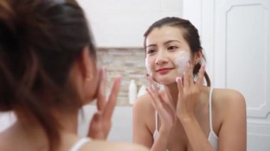 Asyalı kadın banyodaki köpükle deriyi temizler..
