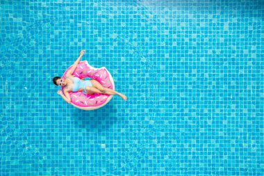 Yüzme havuzunda pembe bir lilo ile mayo giymiş Asyalı genç bir kadının en iyi görüntüsü..
