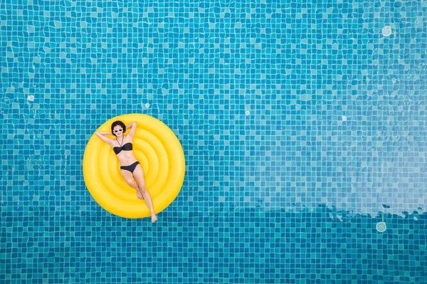 Beautiful young asian woman with yellow inflatable ring relaxing in swimming pool. top view