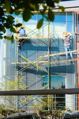 İskele ve inşaat merdivenlerinde yüksek binaların pencerelerini tamir eden adamlar