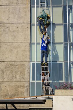 İskele ve inşaat merdivenlerinde yüksek binaların pencerelerini tamir eden adamlar