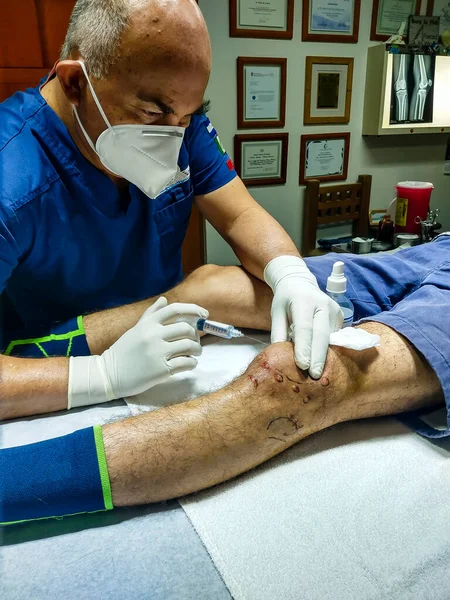 Doktor genç bir erkeğin dizini muayene ediyor.
