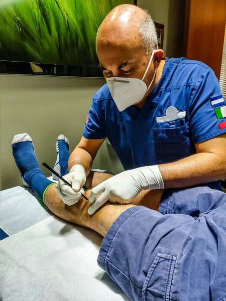 Doktor genç bir erkeğin dizini muayene ediyor.