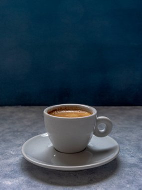 Mavi arkaplan önünde beyaz desenli bir yüzeye kaşık sürülmüş bir fincan kahve. Tepesinde negatif boşluk var..