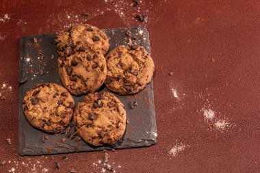 Kahverengi el boyalı arka planda, üzerinde çikolata parçacıkları olan beş kurabiye. Kırsal atmosfer.