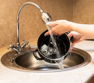 Small metal washbasin with mixer fitted with flexible hose, silver color. female hands hold a container under a stream of water.