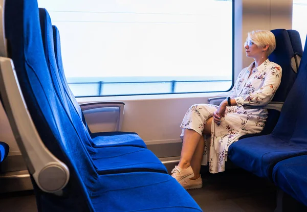A young girl sits alone in a train, high-speed train or electric train carriage with soft, separate seats in blue.