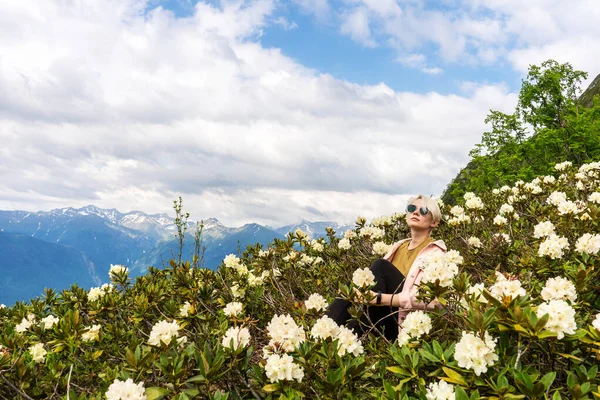A wonderful summer day in the mountains. The green slopes of the mountains are strewn with flowers. A young woman is sitting in flowers.
