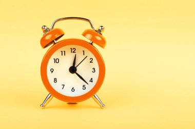 Küçük bir turuncu metal çan retro alarm saatini pastel sarısı arka plan üzerinde fotokopi alanı, düşük açılı ön görüş