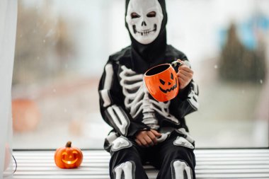 İskelet kostümlü çocuk elinde bardak tutuyor.