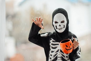 İskelet kostümlü çocuk elinde bardak tutuyor.