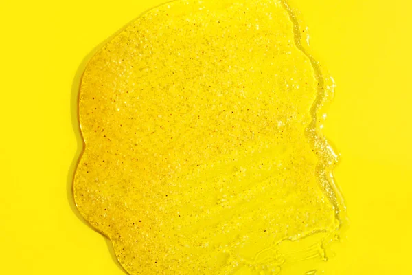 Siero cosmetico o scrub su fondo giallo. Goccia di gel fluido trasparente con particelle. — Foto Stock