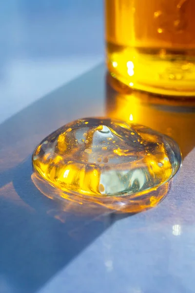 Liquid yellow gel or serum drop on blue background. Transparent macro texture of beauty product. Facial skincare cosmetic
