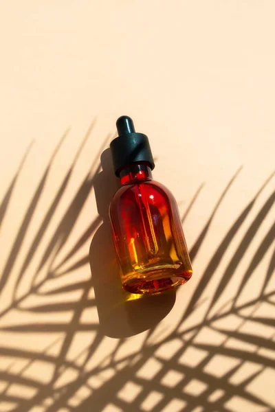 Butelka z pipetą na beżowym tle z cieniem liści palmowych. Produkt kosmetyczny olejek do pielęgnacji skóry, serum — Zdjęcie stockowe