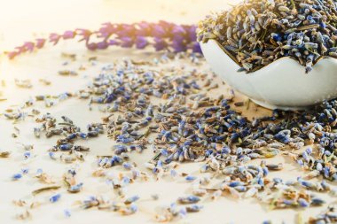 Güneş ışığında ahşap masada kurutulmuş lavanta çiçekleriyle porselen kâse. Sakinleştirici içecek.