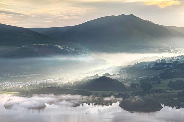 Sabah sevinci, İngiliz Göl Bölgesi 'nde Keswick' i aydınlatırken Derwentwater kıyısındaki erken sislerin içinden geçen ışık huzmeleriyle.