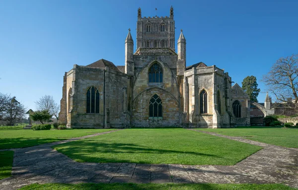 Tewkesbury Manastırı 'nın alçak açılı görüntüsü. Güzel yeşil çimenli, asfaltlı ve berrak mavi gökyüzü.