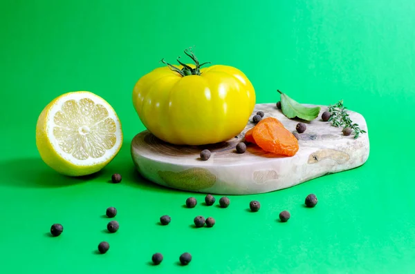 黄色的西红柿、柠檬、胡椒玉米、月桂叶和干杏仁躺在橄榄树木板上，背景是绿色的. — 图库照片
