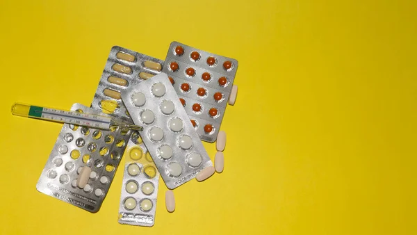 Different medicines in tablets, medical mercury thermometer on yellow