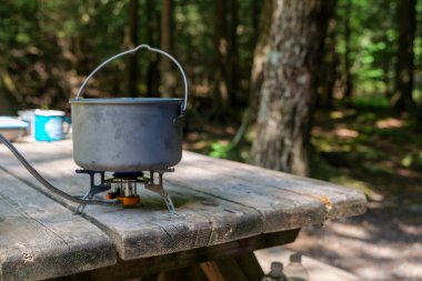 A titanium pot for making food on a gas stove on a camping wooden table in the forest. High quality photo