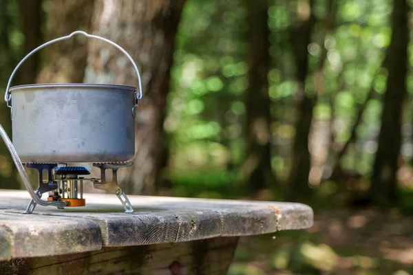 A titanium pot for making food on a gas stove on a camping wooden table in the forest. High quality photo